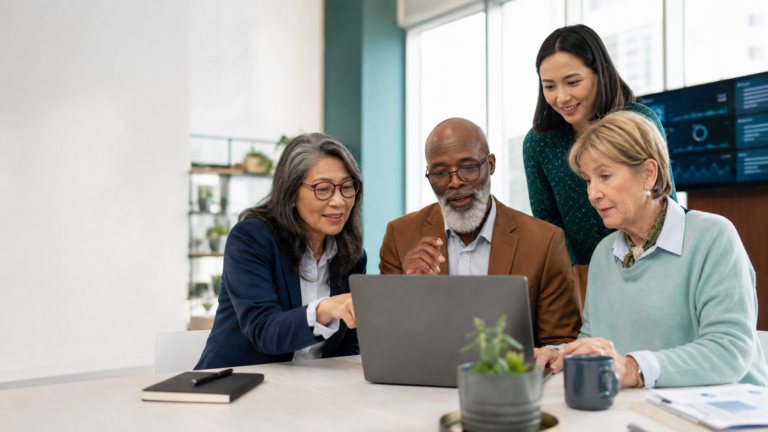 Group photo of a man sitting at a laptop with three female co-workers working with him